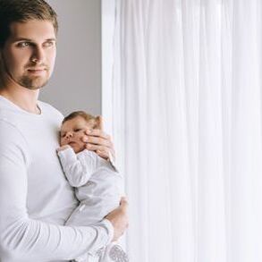 Father holding a baby in front of cleaned hygenic curtains
